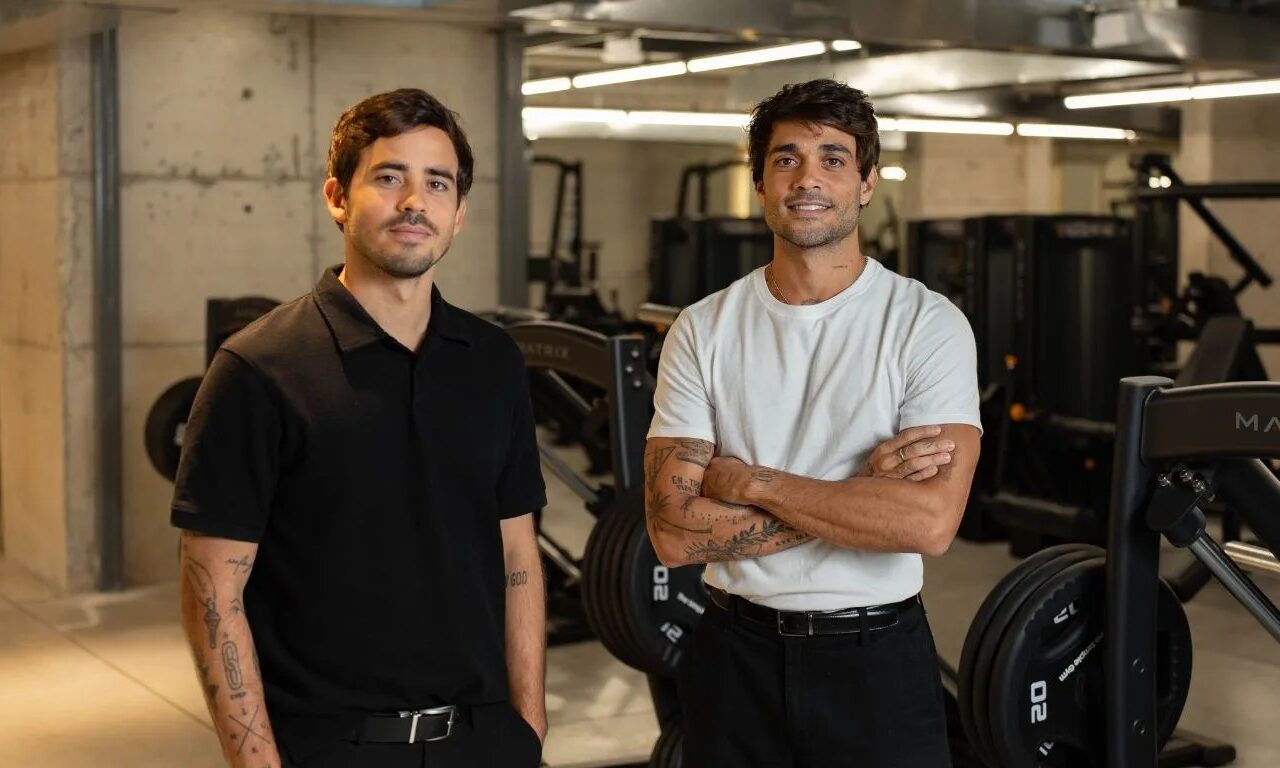Concreto aparente e equipamentos escuros dão o tom sóbrio ao salão de musculação onde a dupla posa