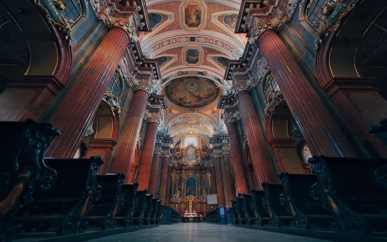 Nave de igreja barroca com forro pintado, colunas e altar ao fundo, em imagem ilustrativa de arte sacra