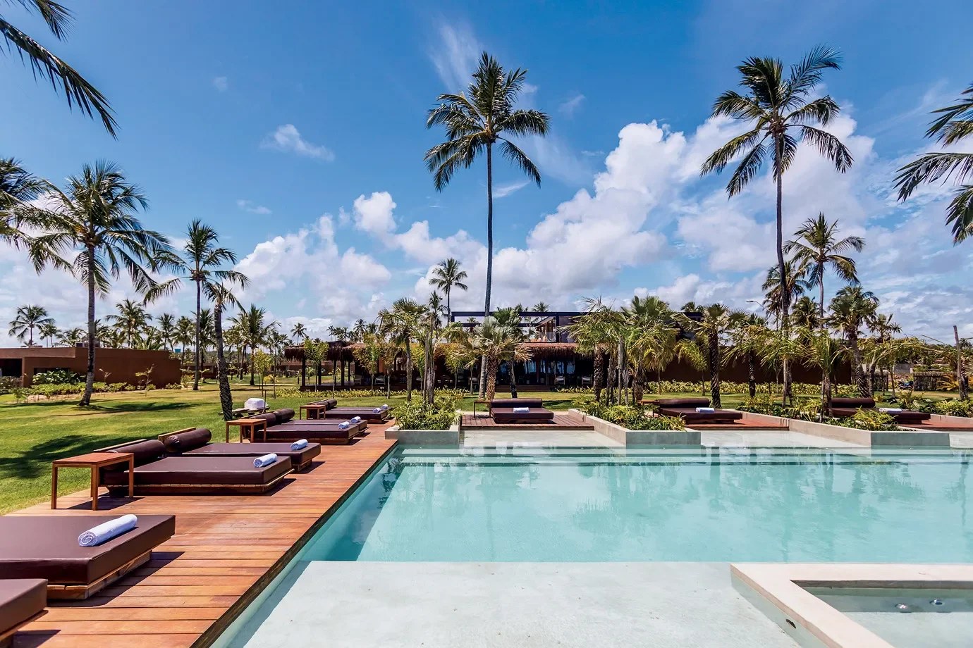 Piscina cercada por deque, espreguiçadeiras e coqueiros em hotel de alto padrão no litoral norte de Alagoas