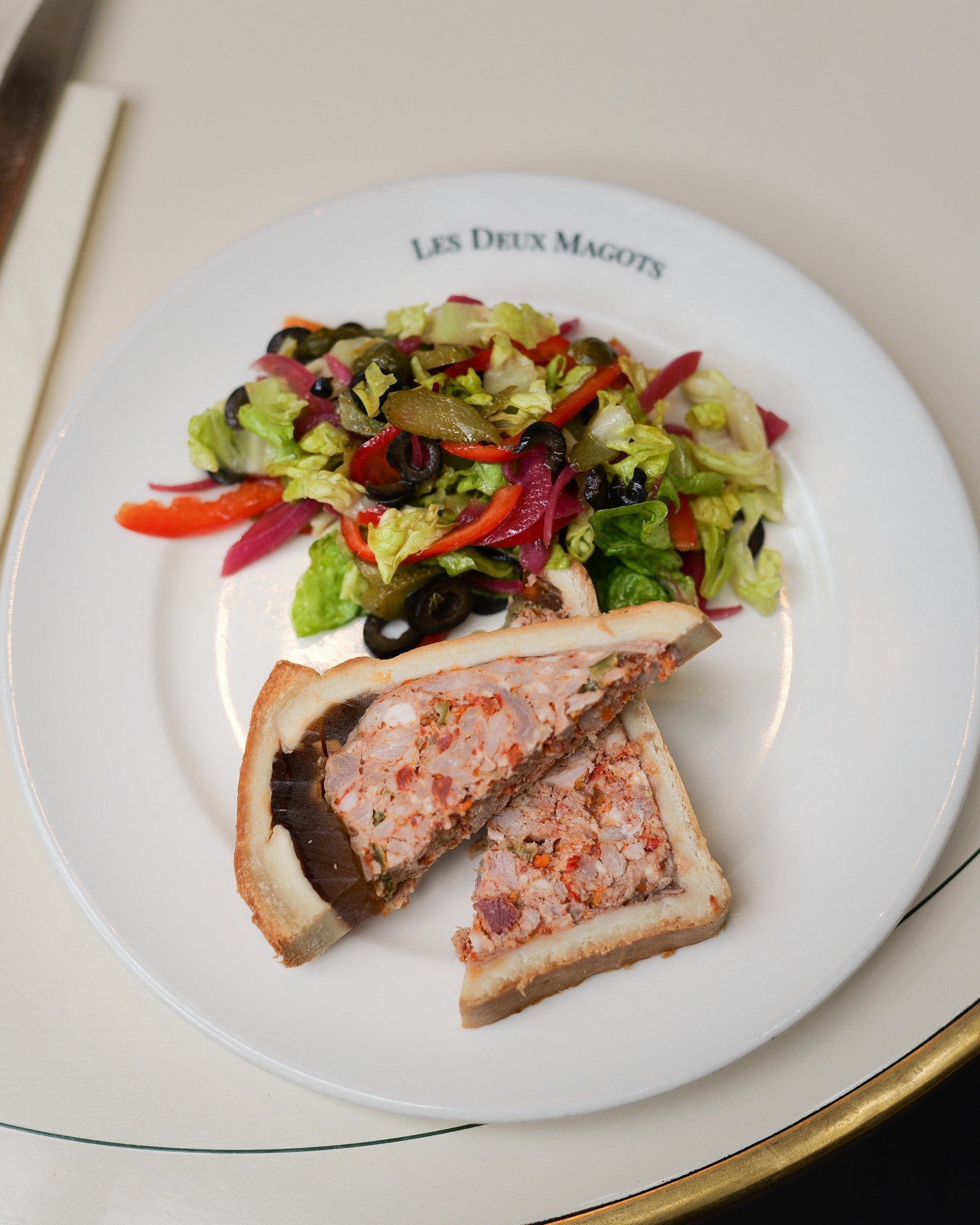Terrina em crosta com salada de azeitonas, servida na louça da casa, na mesa de tampo claro