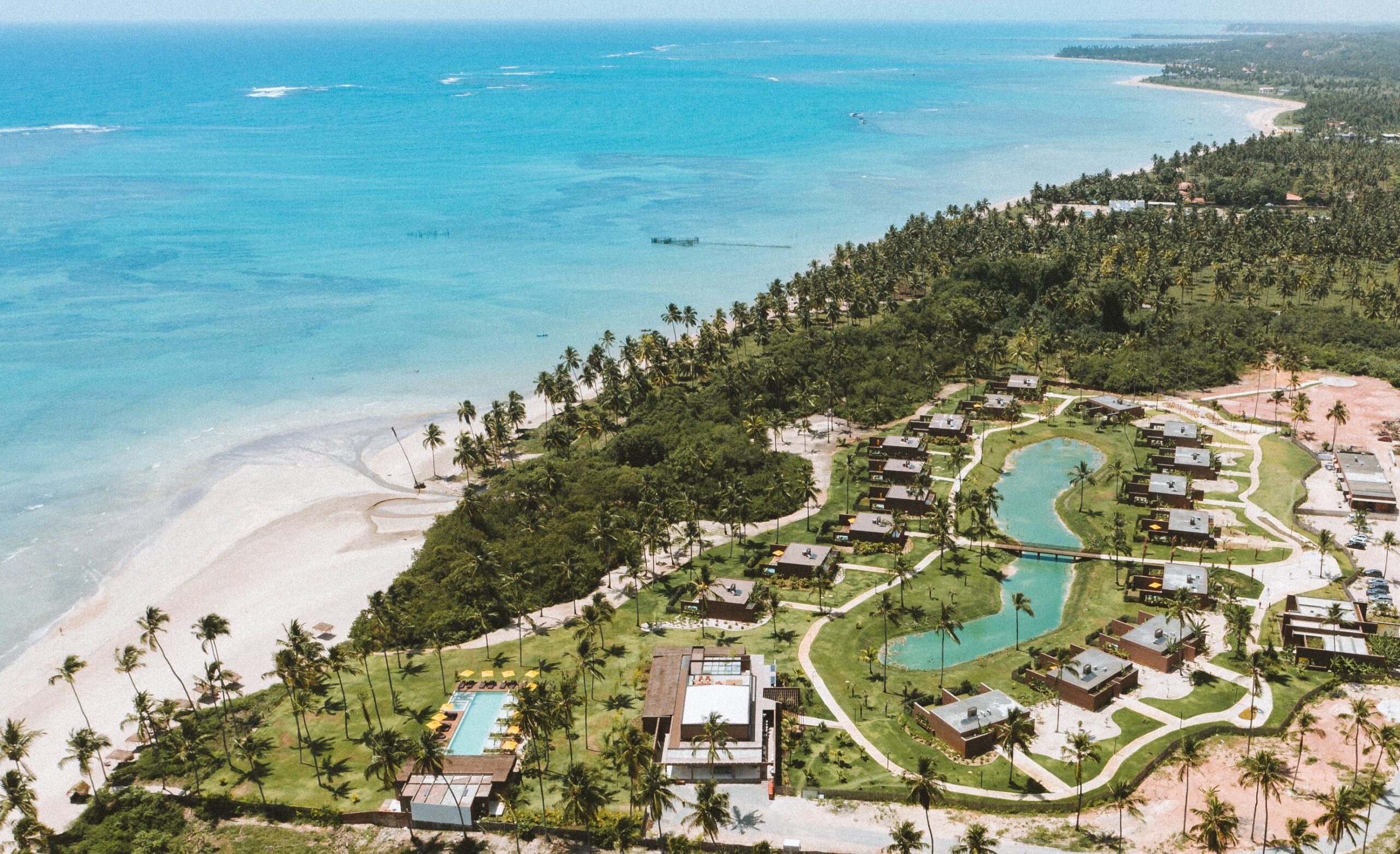 Vista aérea de resort à beira-mar no litoral norte de Alagoas, com chalés, lagoa e mar de águas cristalinas