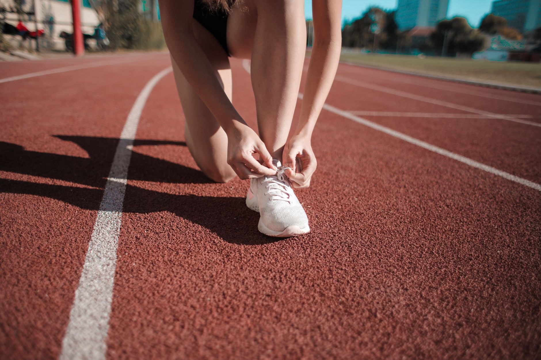 Corredora ajusta o tênis na pista de atletismo, evocando a busca por precisão e performance no esporte