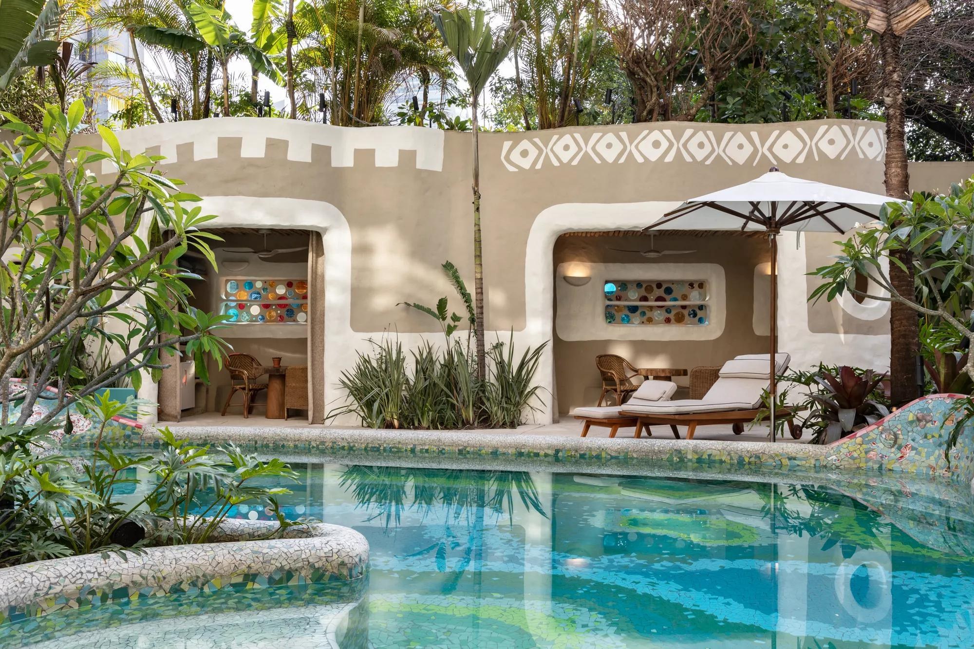 Cabanas de paredes modeladas à mão abrem-se para uma piscina de mosaico, cercada de folhagem