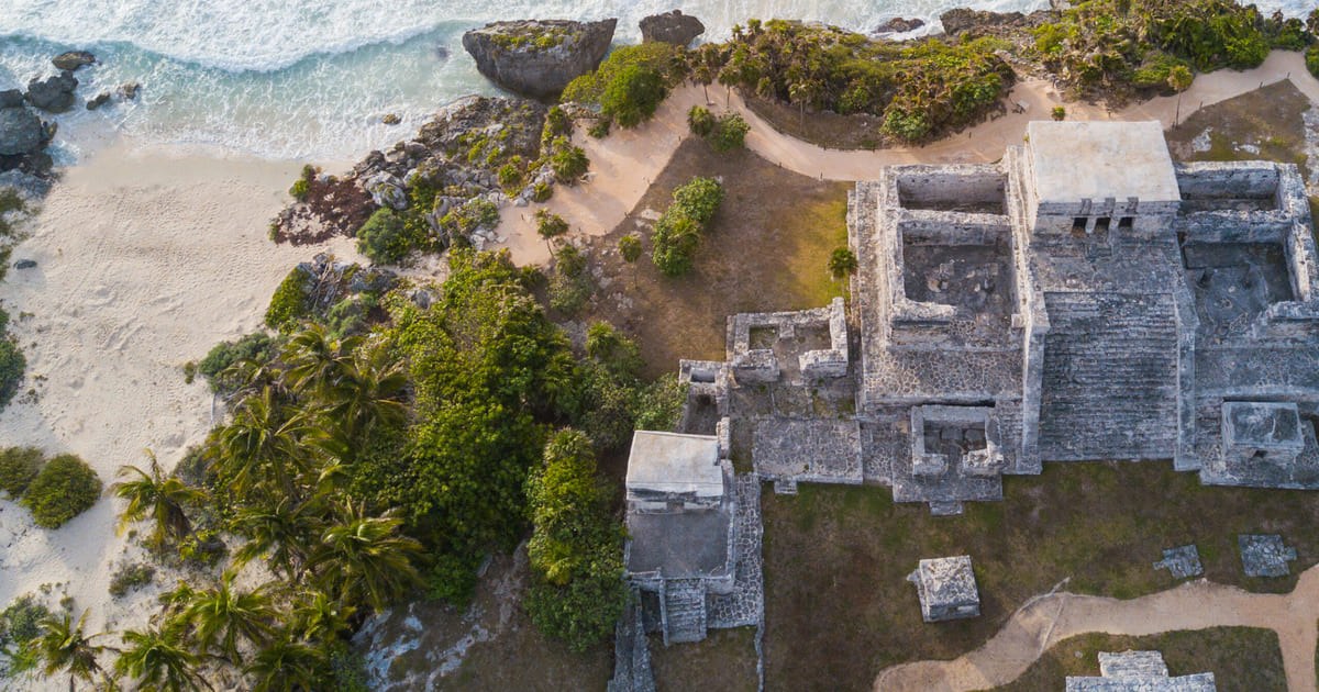 Do alto, o templo de pedra se debruça sobre a faixa de areia clara e as rochas da costa