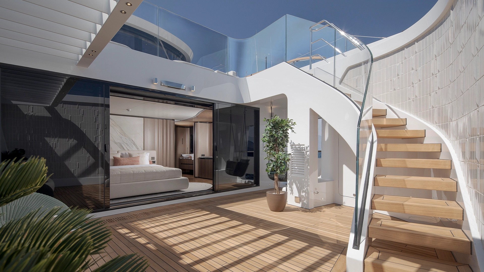 O terraço privativo da proa: as portas de vidro abrem a suíte para o pátio, e a escada leva ao lounge do convés superior