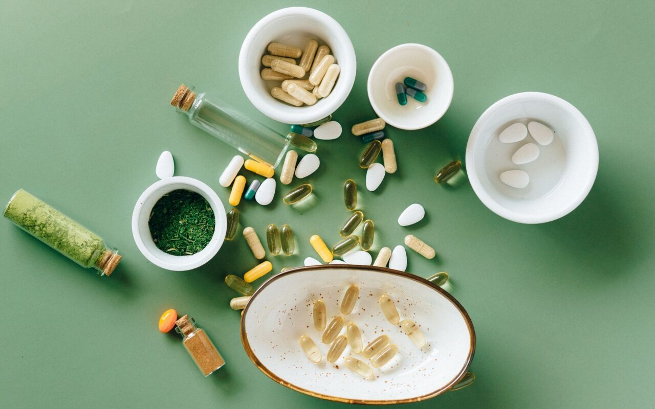 Suplementos, cápsulas e pó de ervas verdes em tigelas ilustram o universo da nutrição funcional e do bem-estar