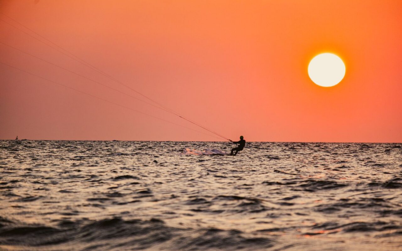 Kitesurfista navega ao pôr do sol, cena associada aos esportes de vento praticados no litoral leste do Ceará