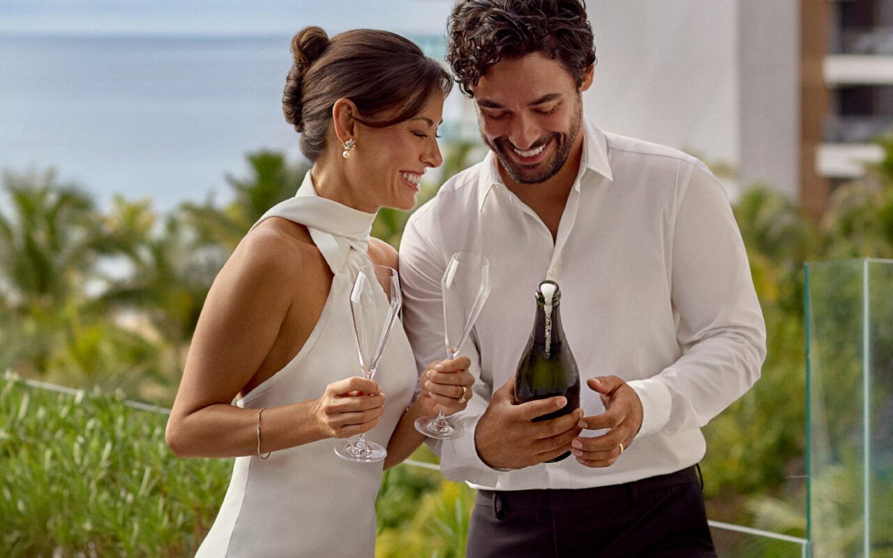 Casal comemora com espumante na varanda com vista para o mar no Waldorf Astoria Riviera Maya